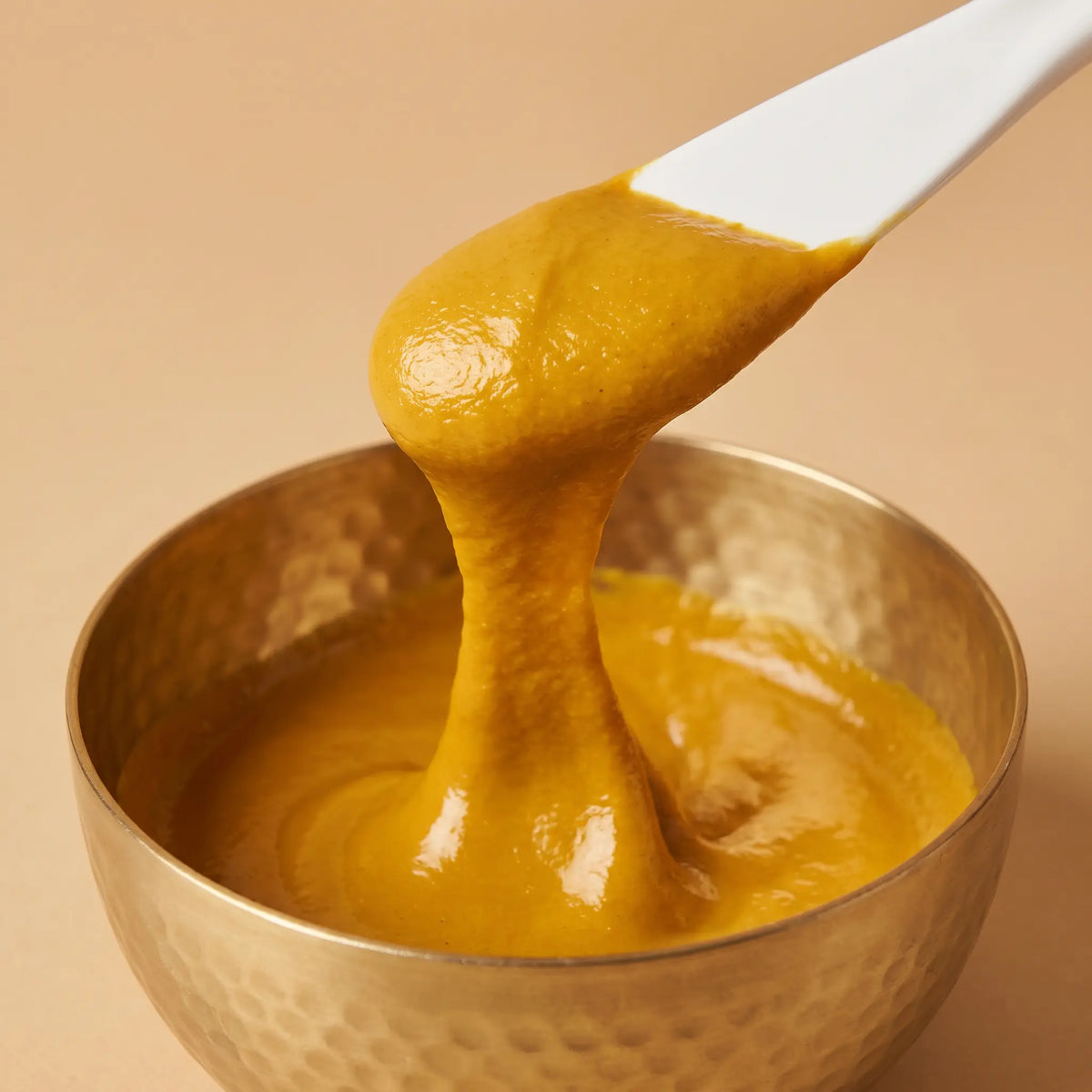 Creamy turmeric paste mixed in a hammered brass bowl